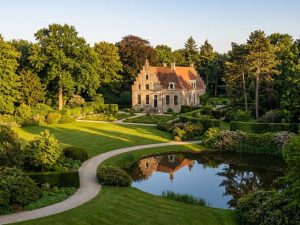 Historisch Nederlands landhuis met klassieke architectuur omringd door weelderige tuin met volwassen bomen in gouden licht