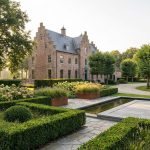 Nederlandse landgoed met klassiek landhuis omringd door professioneel ontworpen tuinen met geometrische hagen en paden.