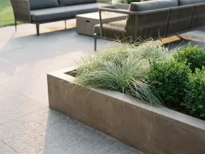 Betonnen plantenbak met siergras en buxushaag op stenen terras met moderne tuinmeubels op de achtergrond