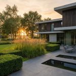 Moderne Nederlandse villa met grote ramen en hedendaagse tuin met geometrische hagen en natuursteen terras