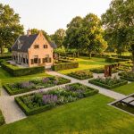 Traditioneel Nederlands landhuis met formele tuinen, gemanicuurde gazons en volwassen bomen in gouden avondlicht