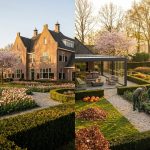 Nederlands landhuis met klassieke architectuur omringd door uitgebreide tuinen met lente- en herfstbeplanting in gouden uurtje