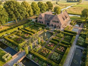 Luchtfoto van Nederlandse villa met geometrische tuinen, pergola en waterpartijen in gouden avondlicht