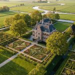 Luchtfoto van elegante Nederlandse villa met geometrische tuinen, kleurrijke bloembedden en weelderig landschap