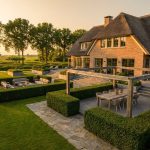 Luxe Nederlandse villa met uitgebreide tuinen, moderne buitenmeubels, pergola en stenen paden in gouden avondlicht