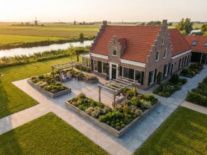 Luchtfoto van elegant Nederlands landhuis met toegankelijke tuin, verhoogde bloembedden en brede paden in gouden uurtje
